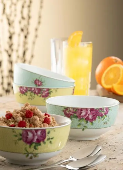 Three decorative bowls filled with cereal, placed on a table with a glass of orange juice and sliced oranges in the background, enhancing a cozy breakfast setting.